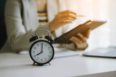 Photo for Alarm clock on the desk. Businesswoman hands using tablet  working in modern office building or home - Royalty Free Image