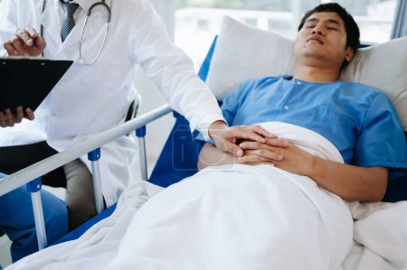Téléchargez les photos : Médecin féminin tenant la main du patient masculin sur le lit avec une solution saline à l'hôpital ou à la clinique - en image libre de droit