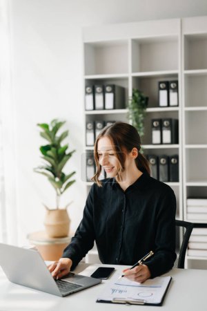 Téléchargez les photos : Expert d'affaires confiant attrayant souriant jeune femme travaillant sur ordinateur portable au bureau dans le bureau créatif - en image libre de droit