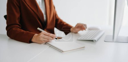 Téléchargez les photos : Femme d'affaires travaillant avec un nouvel ordinateur moderne et écrivant sur le diagramme de stratégie du bloc-notes comme concept à la lumière du matin - en image libre de droit