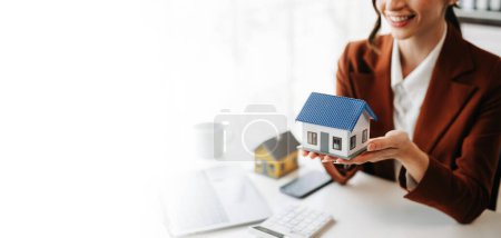 Téléchargez les photos : Femme agent immobilier est utiliser les mains pour protéger le toit rouge pour le concept d'investissement immobilier sur le commerce de la maison, achat au bureau au bureau - en image libre de droit