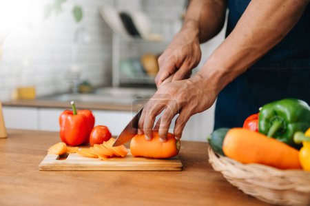 Téléchargez les photos : Fermer les mains du jeune homme qui prépare une salade saine. Découpe de légumes sur une planche à découper sur le comptoir de la cuisine maison. - en image libre de droit