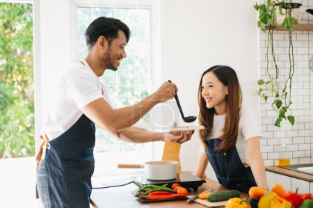Foto de Feliz asiático joven pareja cocinar junto con verduras con pan y fruta en acogedor en madera cocina mesa, amor y valentine - Imagen libre de derechos
