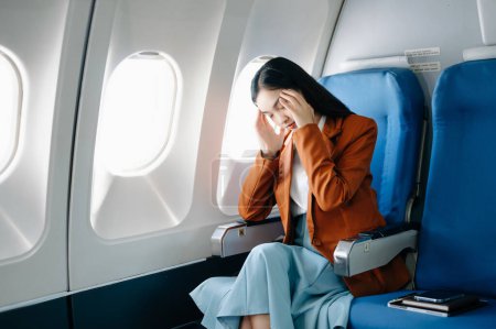 Téléchargez les photos : Photo d'une femme frustrée assise dans un avion, la tête dans les mains. Asiatique femme assis dans un siège dans l'avion - en image libre de droit