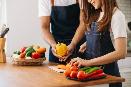 Téléchargez les photos : Un homme dans la cuisine prépare un repas avec du pain et des fruits dans une cuisine confortable tandis que sa femme l'étreint le matin - en image libre de droit