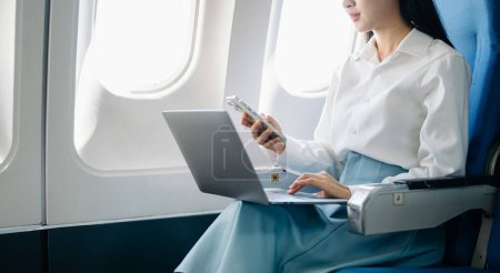 Photo for Attractive Asian female passenger of airplane sitting in comfortable seat while working on laptop computer with mock up area using wireless connection. Travel in style, work with grace - Royalty Free Image