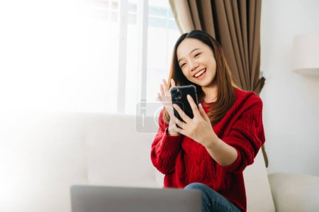 Photo for Asian young woman using the smartphone and  laptop computer on the sofa at home - Royalty Free Image