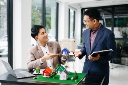 Foto de Vendedor y cliente con modelo de casa en la oficina, Pequeña casa de juguete Pequeña hipoteca Seguro de propiedad y conceptos inmobiliarios - Imagen libre de derechos