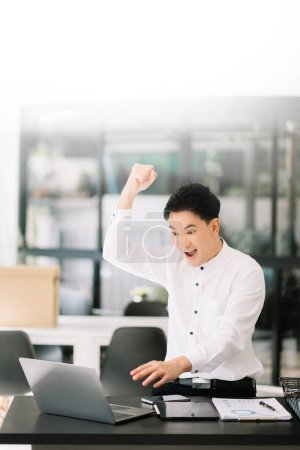 Téléchargez les photos : Homme d'affaires asiatique sont ravis et heureux avec le travail qu'ils font sur ordinateur portable au bureau - en image libre de droit