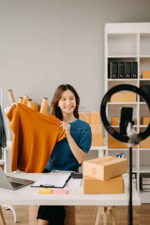 Foto de Concepto de blogger de moda, Mujer joven asiática vendiendo ropa en streaming de video. Puesta en marcha de pequeñas empresas PYME, utilizando smartphone - Imagen libre de derechos