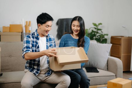 Photo for Young couple with big boxes moving into a new house, new apartment for couple, young asian man and woman helping to lift boxes on sofa for the new home, Moving house - Royalty Free Image