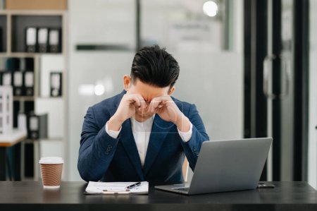 Téléchargez les photos : Frustré jeune homme d'affaires travaillant sur un ordinateur portable assis à son lieu de travail dans le bureau - en image libre de droit