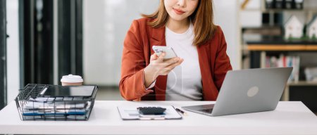 Photo for Young beautiful woman working on smartphone and  laptop while sitting at the wooden table modern office - Royalty Free Image