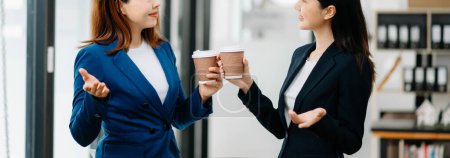 Téléchargez les photos : Heureuses deux femmes d'affaires asiatiques tenant des tasses à café au bureau - en image libre de droit
