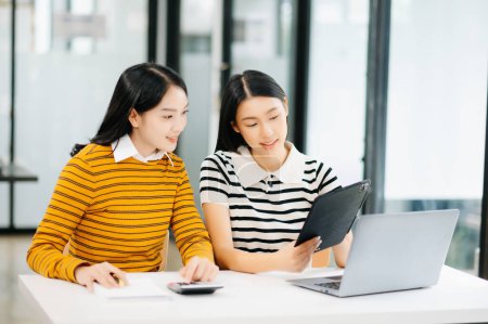 Foto de Dos atractivas jóvenes asiáticas estudiantes universitarias que trabajan en el proyecto escolar usando tableta digital juntas, disfrutan hablando por la mañana - Imagen libre de derechos