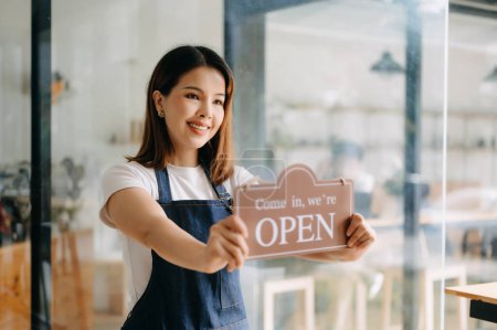 Téléchargez les photos : Jeune femme asiatique propriétaire de café tenant signe ouvert prêt à recevoir des commandes dans le café - en image libre de droit
