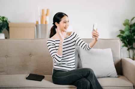 Téléchargez les photos : Jeune femme asiatique se détendre sur un canapé confortable à la maison textos sur smartphone - en image libre de droit
