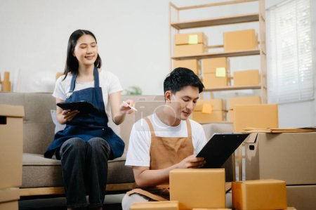 Photo for Young couple starting small business in home office. SME owners check online orders using tablet pc and packing boxes for delivery. Freelance work at home - Royalty Free Image