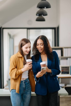 Téléchargez les photos : Heureuses deux jeunes femmes d'affaires tenant des tasses à café dans un bureau de co-working - en image libre de droit
