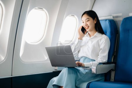 Photo for Attractive Asian female passenger of airplane sitting in comfortable seat while working on laptop computer,  using wireless connection. Travel in style, work with grace - Royalty Free Image