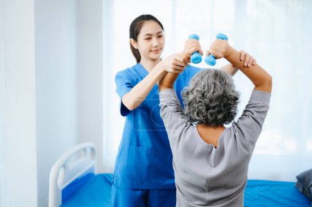 Photo for Asian physiotherapist helping female patient stretching arm during exercise correct with dumbbell in hand in hospital office - Royalty Free Image