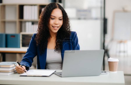 Photo for Beautiful African businesswoman using laptop sitting at her working place. Concentrated at work. - Royalty Free Image