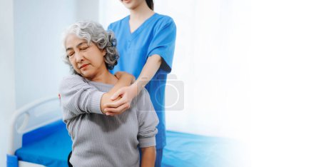 Foto de Fisioterapeuta asiática ayudando a paciente femenina a estirar el brazo durante el ejercicio en la oficina del hospital - Imagen libre de derechos