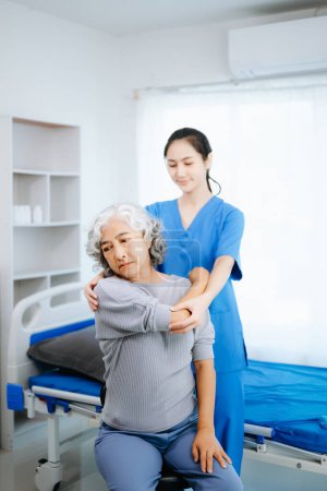 Photo for Asian physiotherapist helping female patient stretching arm during exercise in hospital office - Royalty Free Image