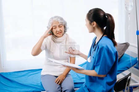 Foto de Médico asiático tomando notas mientras examina paciente anciana asiática en el hospital - Imagen libre de derechos
