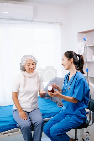 Photo for Asian doctor in white suit take notes while discussing and Asian elderly, woman patient  on bed with receiving saline solution in hospital or clinic - Royalty Free Image