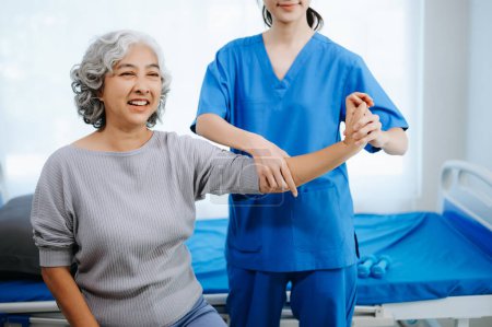 Foto de Fisioterapeuta asiática ayudar a paciente femenina brazo de estiramiento durante el ejercicio correcto con mancuerna en la mano en la oficina del hospital - Imagen libre de derechos