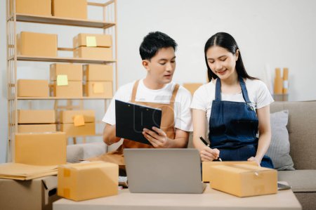 Photo for Young couple starting small business in home office. SME owners check online orders using tablet pc and packing boxes for delivery. Freelance work at home - Royalty Free Image