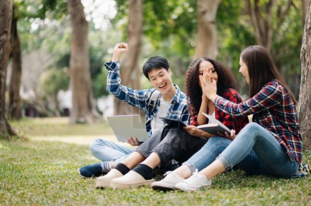 Photo for Young college students studying together in campus park. Happy friends celebrating success of their project - Royalty Free Image