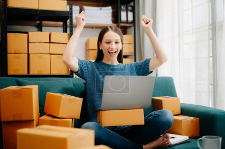 Photo for Young female business owner using laptop and preparing parcels for sending online orders to customer in home office. Shopping Online concept - Royalty Free Image