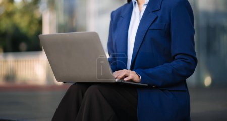Téléchargez les photos : Jeune femme d'affaires travaillant sur un ordinateur portable dans la rue, arrière-plan du centre d'affaires. - en image libre de droit