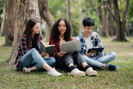 Photo for Diverse students studying sitting under tree the campus park. Young people are spending time together reading book and using tablet pc. Education and communication concept - Royalty Free Image