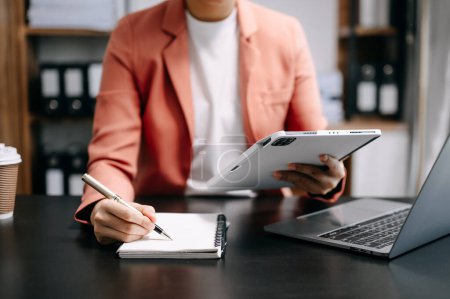 Téléchargez les photos : Photo recadrée de femme d'affaires travaillant avec un nouvel ordinateur moderne et l'écriture dans le bloc-notes - en image libre de droit
