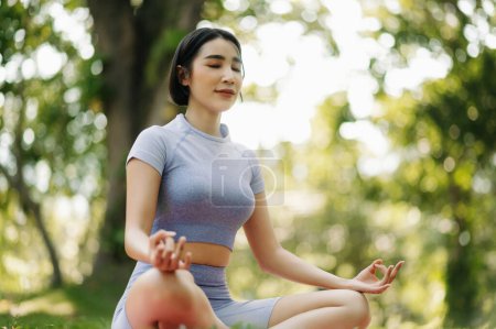 Téléchargez les photos : Asiatique jeune femme méditant assis dans la pose de lotus dans le jardin d'été. Concept de paix intérieure et de pleine conscience - en image libre de droit
