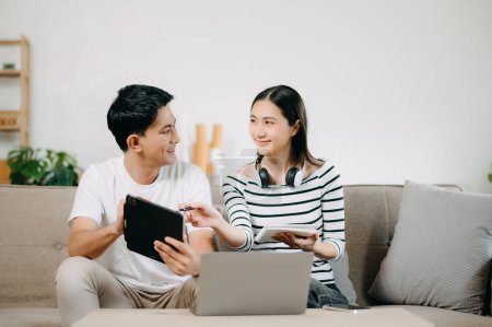 Photo for Asian Female discussing new project with male colleague. Young woman talking with young Asian man with financial on sofa in home office - Royalty Free Image