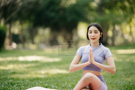 Téléchargez les photos : Portrait de jeune femme pratiquant le yoga dans un parc d'été, fond d'arbres flous. Style de vie sain et concept de relaxation - en image libre de droit