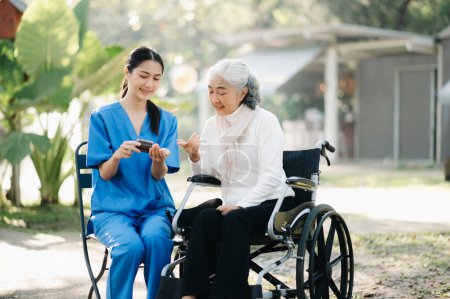 Photo for Young Asian nurse giving pills to senior woman on wheelchair in hospital park. Senior healthcare concept - Royalty Free Image