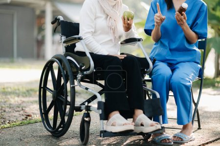 Téléchargez les photos : Personnes âgées asiatique femme âgée en fauteuil roulant avec soignant asiatique soignant dans le jardin. avec les soins d'un soignant et d'une assurance maladie pour personnes âgées - en image libre de droit