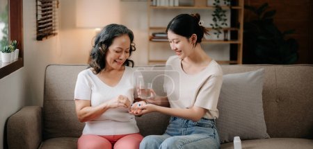 Téléchargez les photos : Jeune femme asiatique prenant soin d'une femme âgée, donnant un verre d'eau médecine quotidienne ou des suppléments vitaminiques, soins de santé aux personnes âgées - en image libre de droit