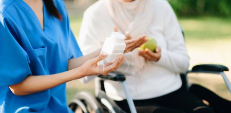 Photo for Young nurse giving pills to senior woman on wheelchair in hospital park. Senior healthcare concept - Royalty Free Image