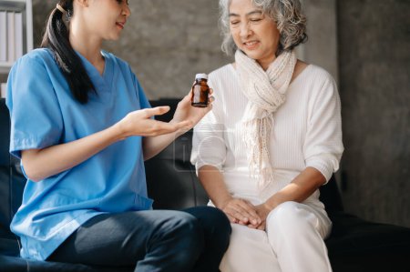Foto de Médico asiático explicar el uso de medicamentos a la mujer. Médico y paciente en el sofá en casa - Imagen libre de derechos