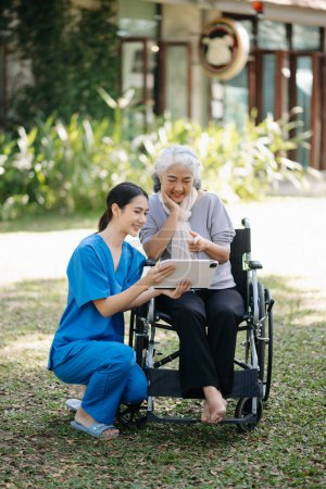 Anciana mujer mayor asiática en silla de ruedas con cuidador asiática cuidadosa y animar a los pacientes en el jardín. con el cuidado de un cuidador y un seguro de salud para personas mayores