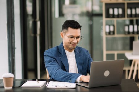 Foto de Joven hombre atractivo utilizando el ordenador portátil en el lugar de trabajo. Concentrado en el trabajo en la oficina - Imagen libre de derechos