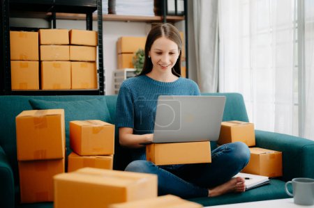 Photo for Young business owner woman prepare parcel box and standing check online orders for deliver to customer on laptop Shopping Online concept. on sofa at home office - Royalty Free Image