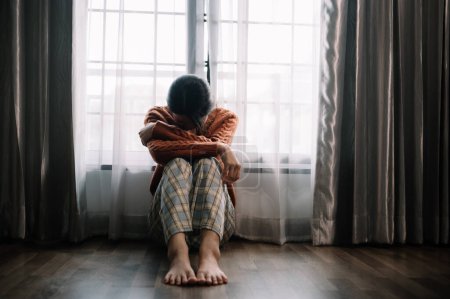 Téléchargez les photos : Asiatique femme sentiment dépression assis sur le sol à la fenêtre dans la maison - en image libre de droit