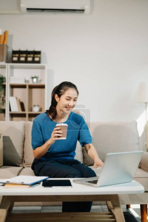 Photo for Asian Business woman using laptop with a smile while sitting on sofa at home office - Royalty Free Image